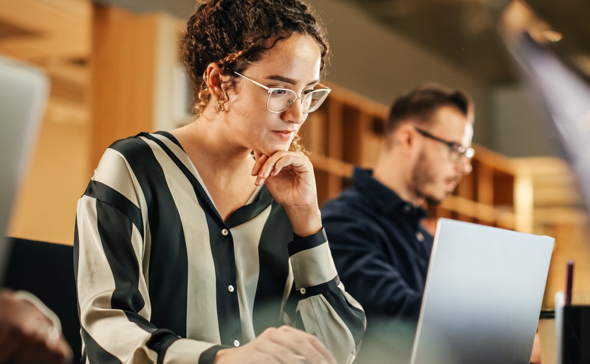 Woman in a striped top reviewing documents at a laptop, payroll compliance services